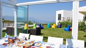 An outdoor dining area with a table set for a meal, surrounded by colorful bean bags and wicker furniture, overlooking a scenic view.