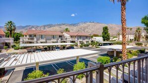 Un hotel con piscina, palmeras y montañas al fondo.