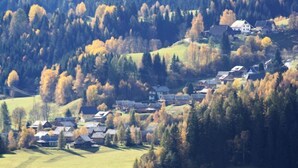 A rural village with houses clustered on a hillside, surrounded by dense forests.