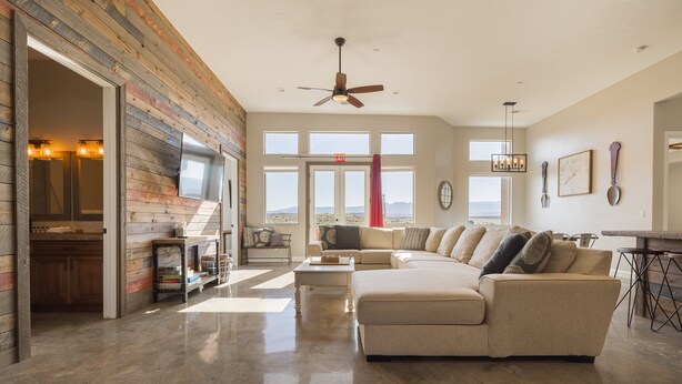 A spacious living room with a large sectional sofa, a ceiling fan, and a view of the desert through large windows.