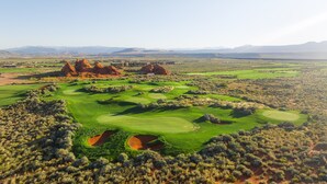 A golf course with multiple greens and bunkers, surrounded by desert vegetation and red rock formations.