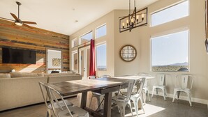 A spacious living area with a large wooden wall, a dining table with chairs, a sofa, and a TV mounted on the wall.