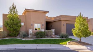 A modern two-story house with a flat roof, a garage, and a well-maintained front yard with various shrubs and a lawn.