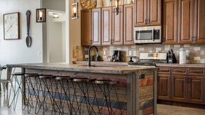 A kitchen with wooden cabinets, a central island with stools, a microwave, and a coffee maker.