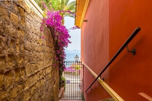 Une ruelle étroite, bordée d’un côté par un mur de pierre et de l’autre par un bâtiment rouge.