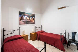 Un dormitorio con dos camas, una mesita de noche de madera, una silla y un cuadro en la pared.