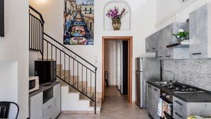 A modern kitchen with a built-in stove, a microwave, and a refrigerator. There is a staircase leading to another level, and a painting of a street scene is visible on the wall. - Ciuri Ciuri in Noto With 3 Bedrooms and 2 Bathrooms (Noto)