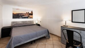 A hotel room with a bed, a desk, a chair, a lamp, and a framed picture on the wall. - Ciuri Ciuri in Noto With 3 Bedrooms and 2 Bathrooms (Noto)