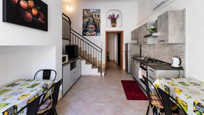 A modern kitchen with a stove, sink, and microwave. There is a dining area with a table and chairs. A staircase leads to another room. - Ciuri Ciuri in Noto With 3 Bedrooms and 2 Bathrooms (Noto)