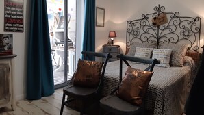 A cozy bedroom with a bed, two chairs, a nightstand, and a window with curtains.