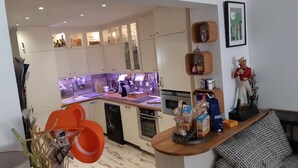 A modern kitchen with built-in appliances, a dining area with a patterned sofa, and a decorative figure on a shelf.