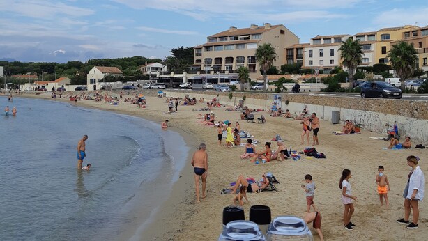 A beach with people, a table with glasses and cutlery, and buildings in the background.