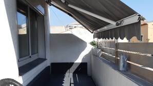 A narrow balcony with a chair, a small table, and a covered area.