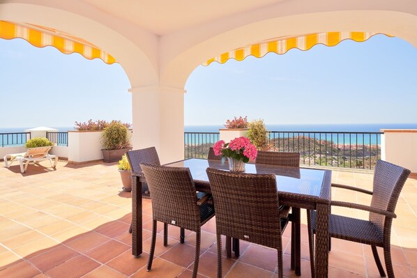 Eine Terrasse mit Tisch und Stühlen, Blumentöpfen und Blick auf das Meer.