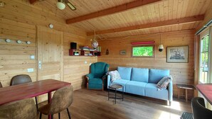 A wooden cabin interior with a dining table, chairs, a sofa, a small table, a globe, books, and a window with a view of greenery. - Intimate, sunny châlet for 2 people in southern Normandy (Saint-Mars-d'Égrenne)
