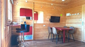 A compact kitchen with a microwave, red cabinets, and a dining area with a table and chairs. - Intimate, sunny châlet for 2 people in southern Normandy (Saint-Mars-d'Égrenne)