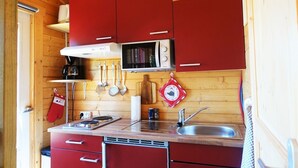 A compact kitchen with red cabinets, a microwave, a stove, and a sink. - Intimate, sunny châlet for 2 people in southern Normandy (Saint-Mars-d'Égrenne)