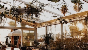 A restaurant with a checkered floor, wooden tables, wicker chairs, and hanging plants. - Hôtel Rose Thé (La Ciotat)