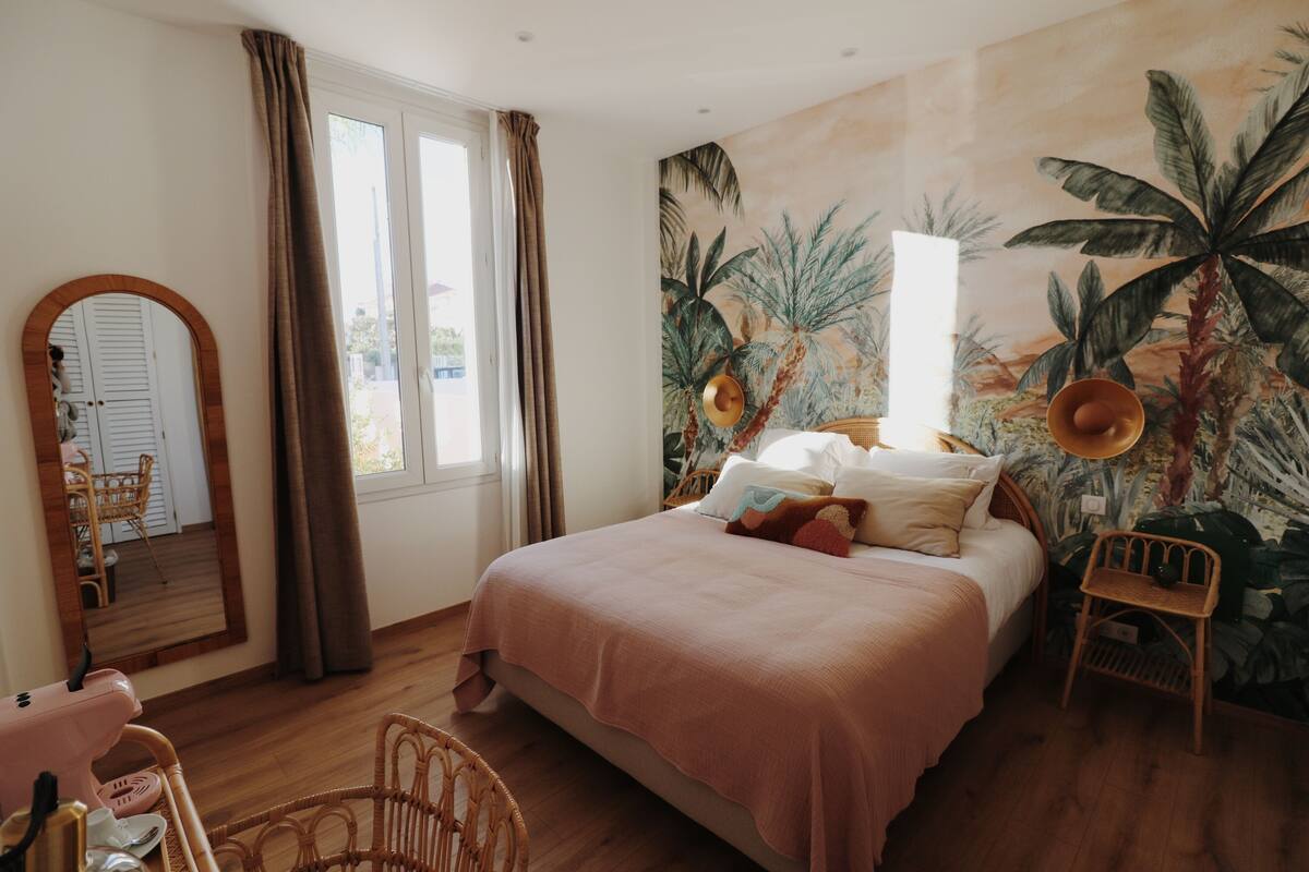 A bedroom with a large bed, a mirror, and a tropical mural on the wall.