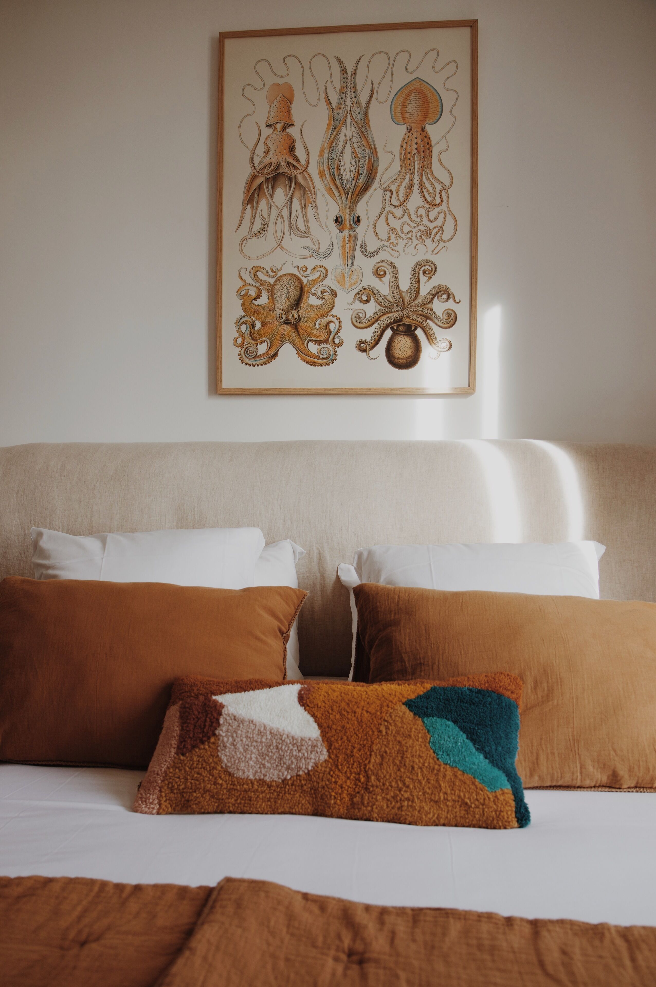 Een slaapkamer met een bed, kussens en een lijst met een kunstwerk aan de muur.