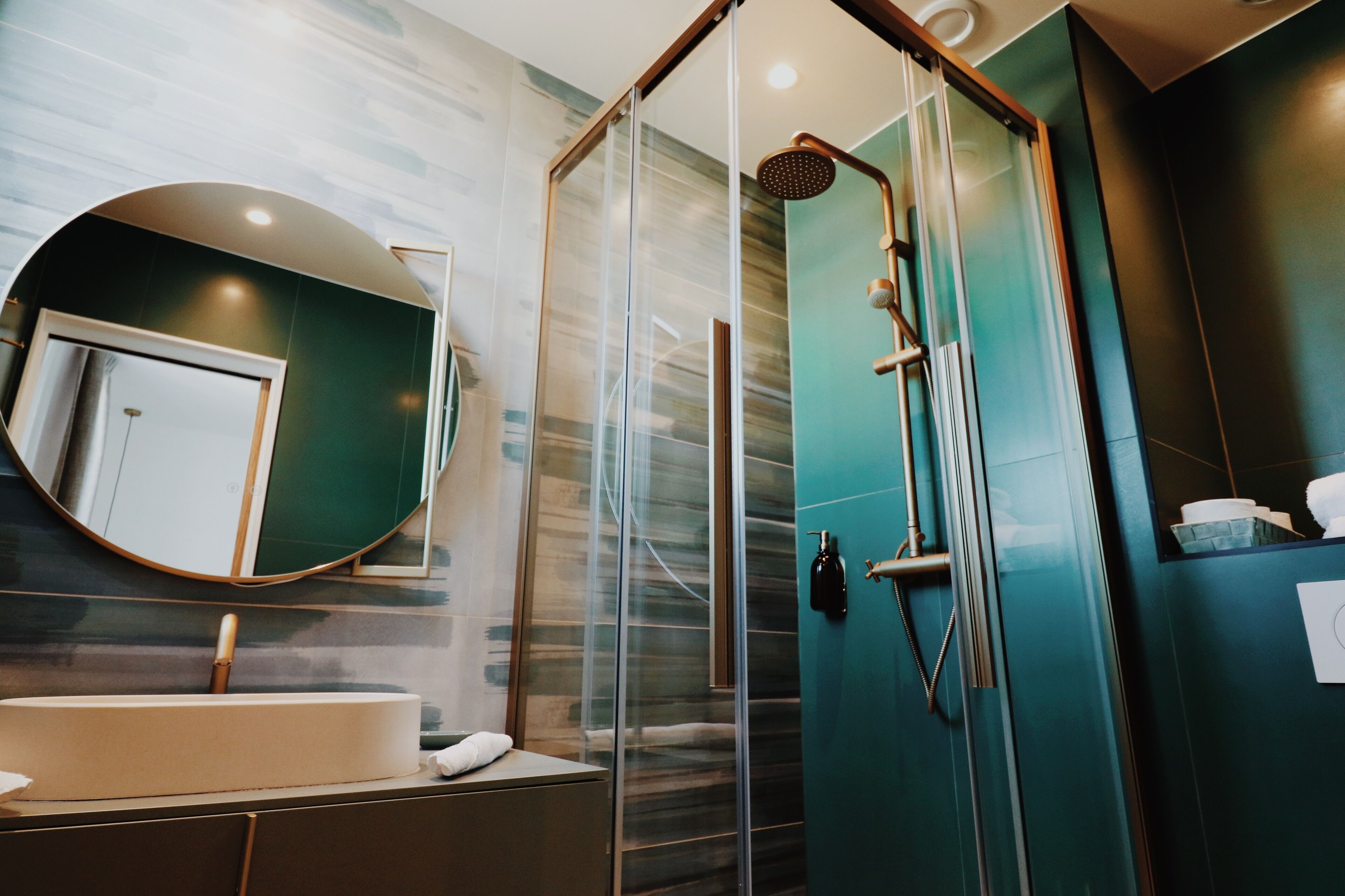 A modern bathroom with a glass-enclosed shower, a round mirror, and a white sink.