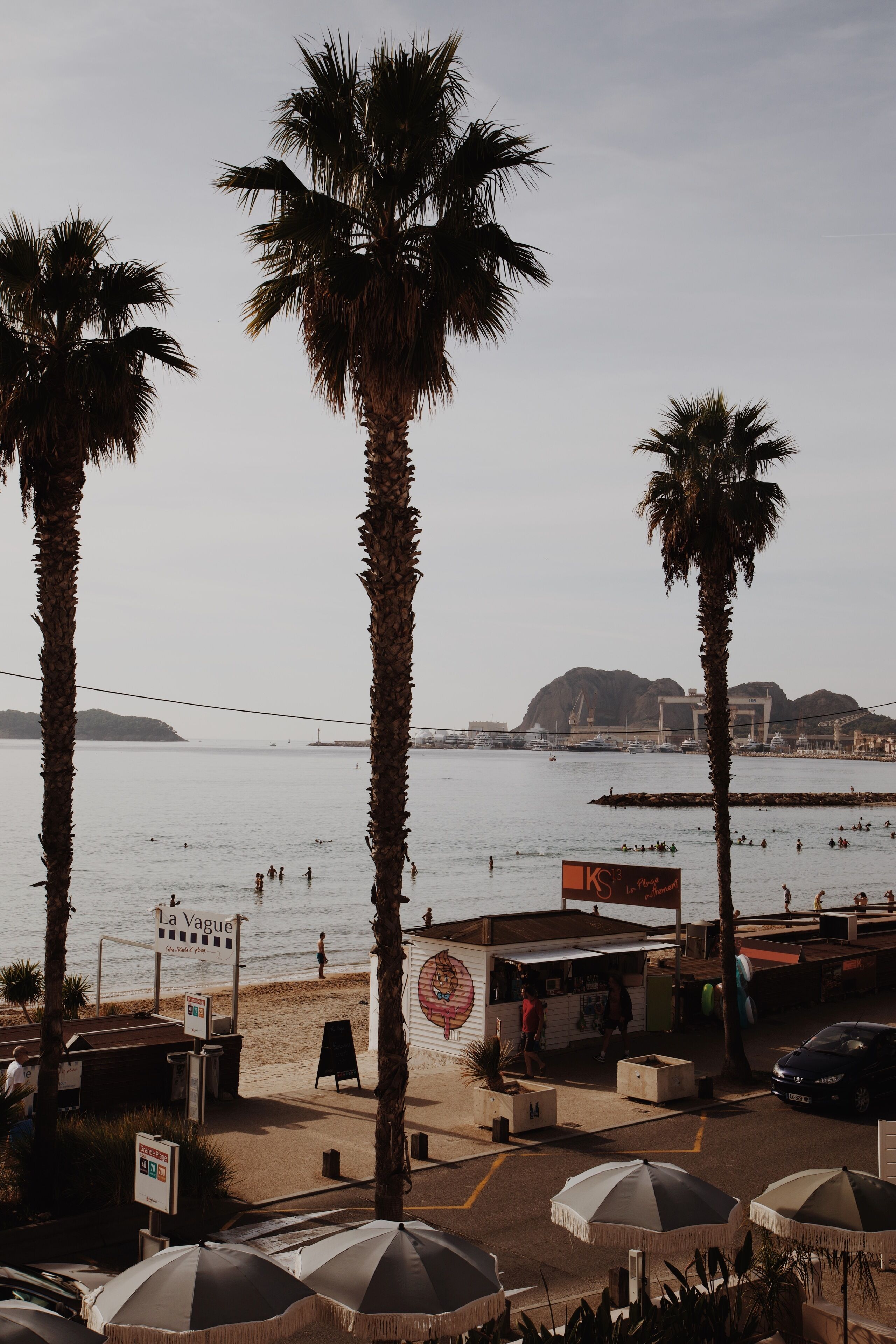 Une vue sur la plage, avec des palmiers, un kiosque et des parasols.