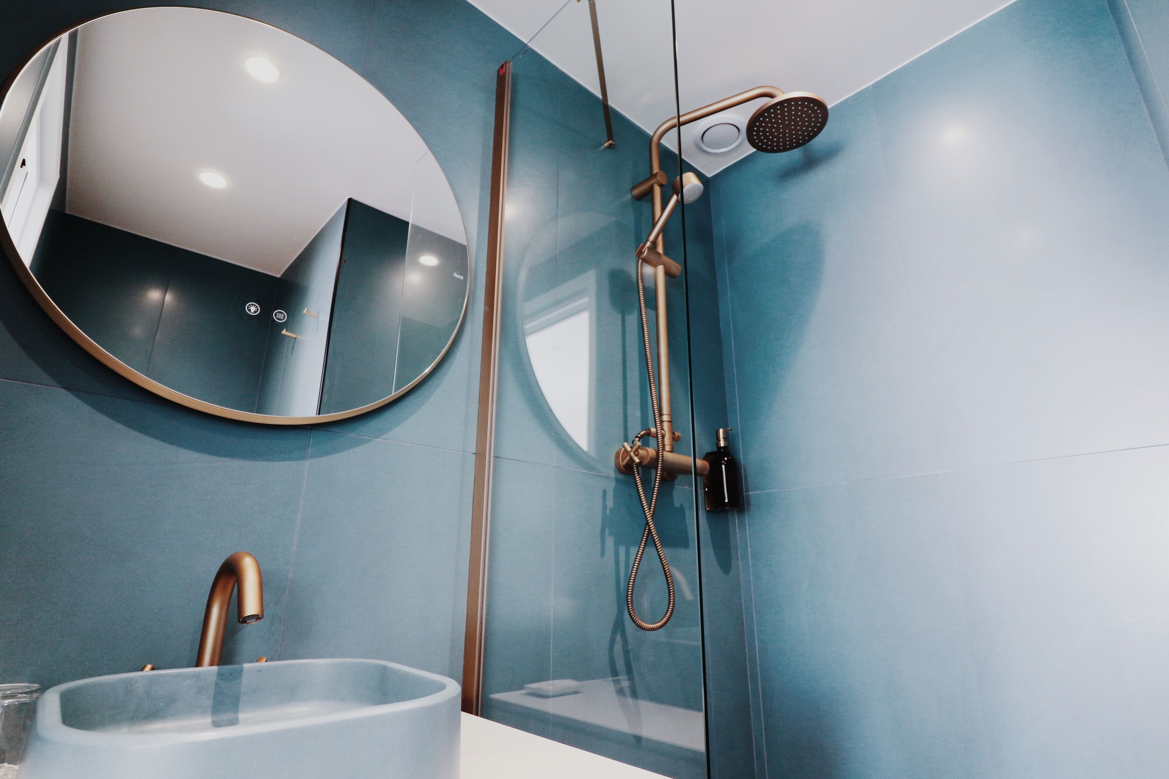 Une salle de bain moderne avec un grand miroir rond, un lavabo en verre et une douche équipée d’un pommeau de douche à main.
