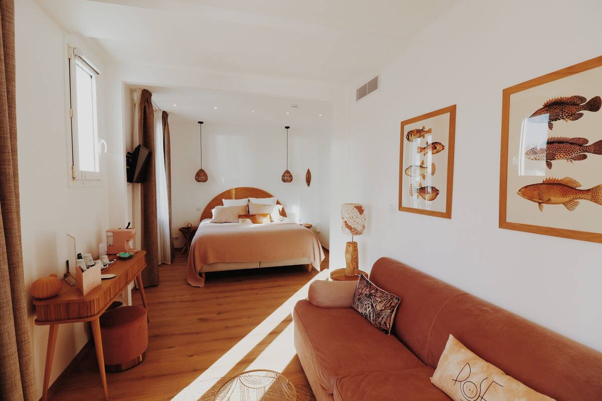 A modern bedroom with a bed, a wooden desk, a brown sofa, and framed fish artwork on the walls.