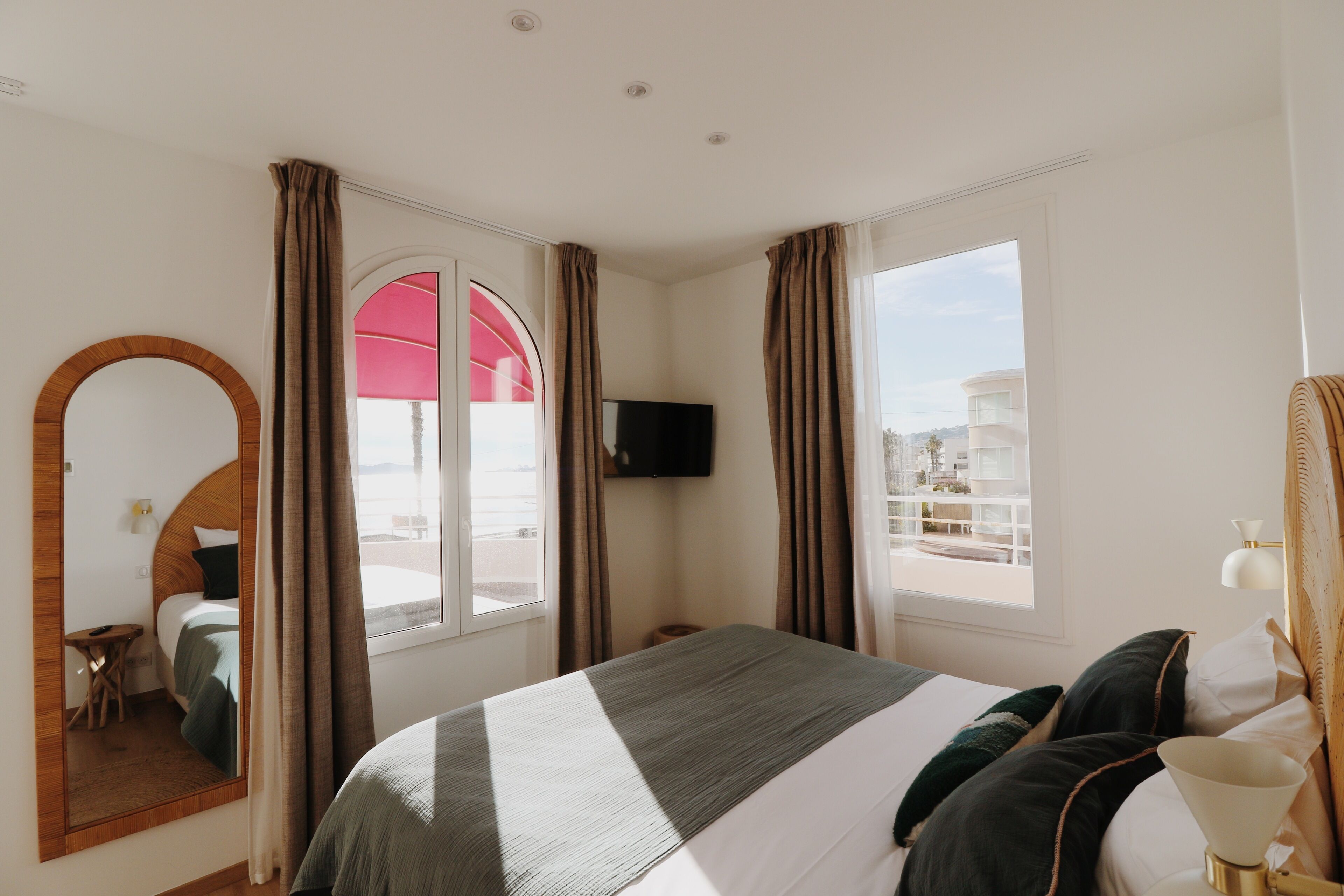 A hotel room with a bed, a TV, a large mirror, and a window with curtains.