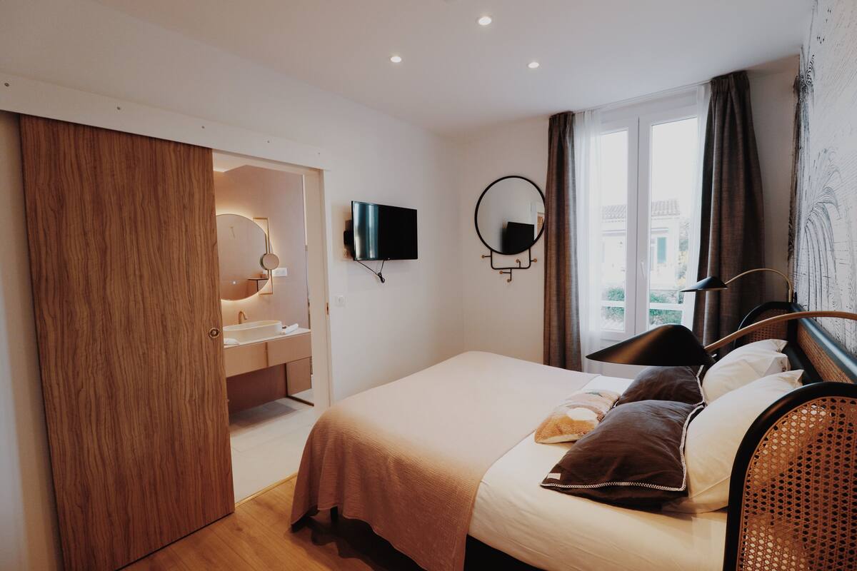 A hotel room with a bed, a TV, a mirror, and a window with curtains.