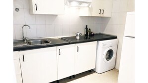 Ett kompakt kök med vita skåp, en svart bänkskiva, ett handfat, en tvättmaskin och ett kylskåp.