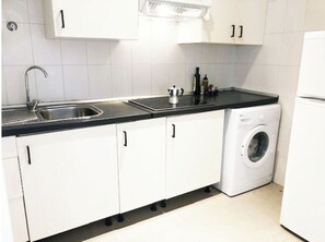 A compact kitchen with white cabinets, a black countertop, a sink, a washing machine, and a refrigerator.