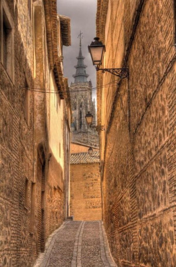 A narrow alleyway with stone walls and a cobblestone path leading to a historic building with a tower.