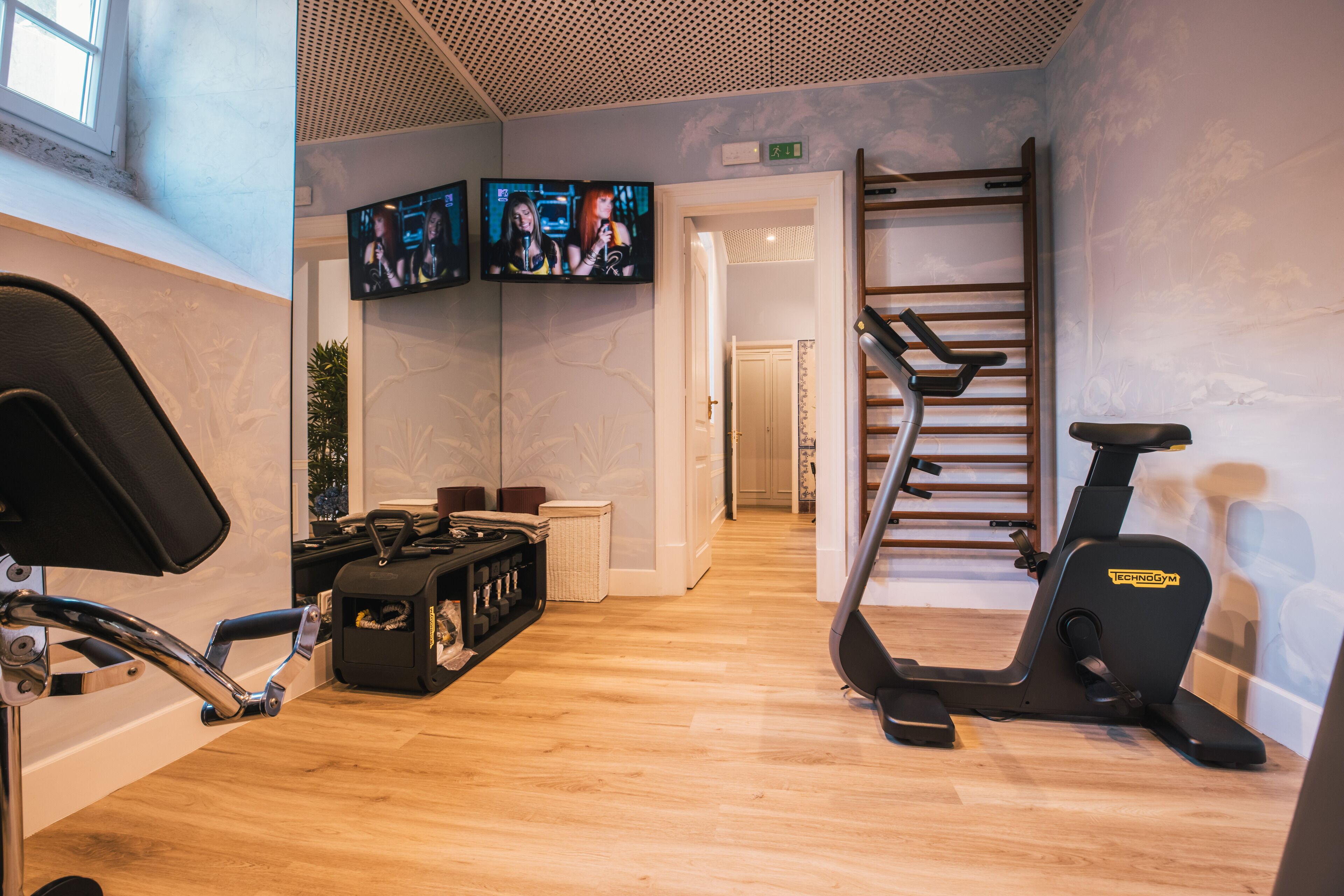 A gym with exercise equipment, a TV mounted on the wall, and a wooden floor.
