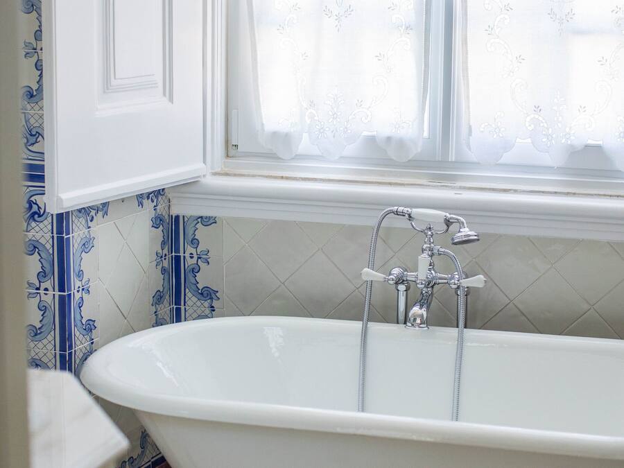 A bathroom with a freestanding bathtub, a window with curtains, and blue and white patterned tiles.