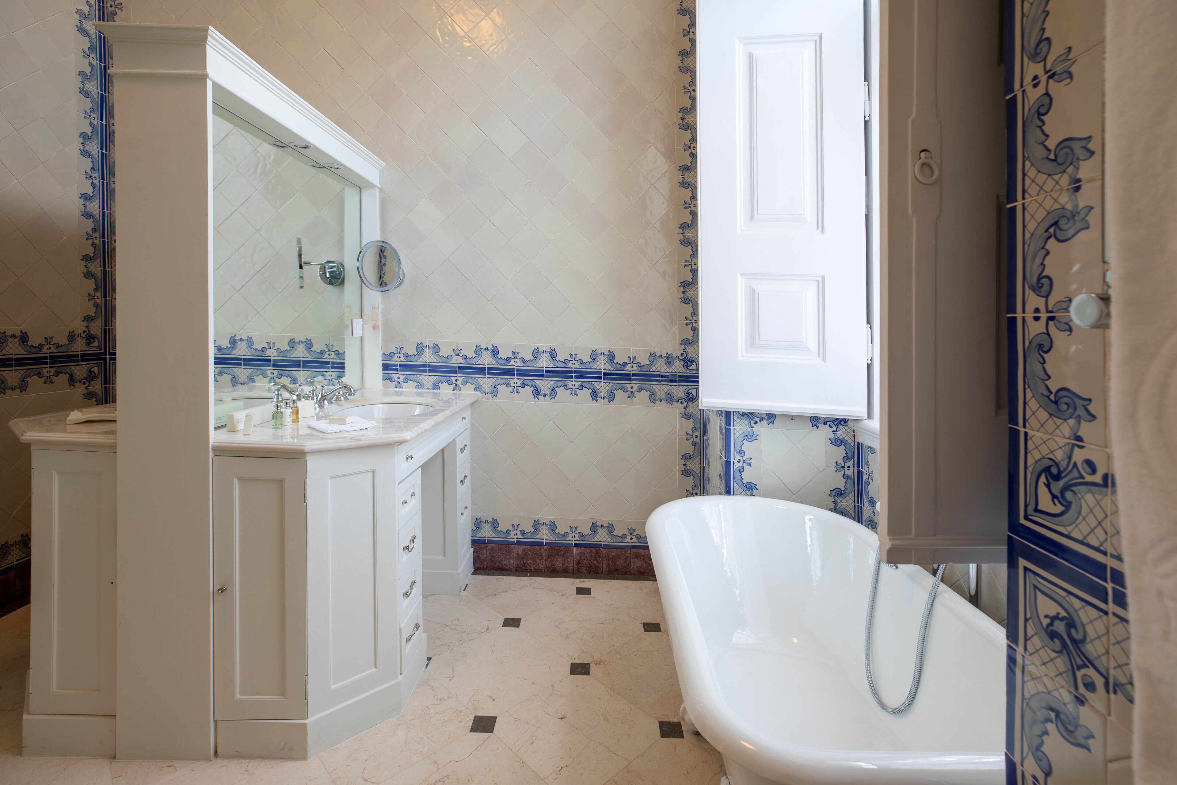 Une salle de bain avec une baignoire blanche, un meuble-lavabo avec un miroir et des carreaux décoratifs sur les murs.