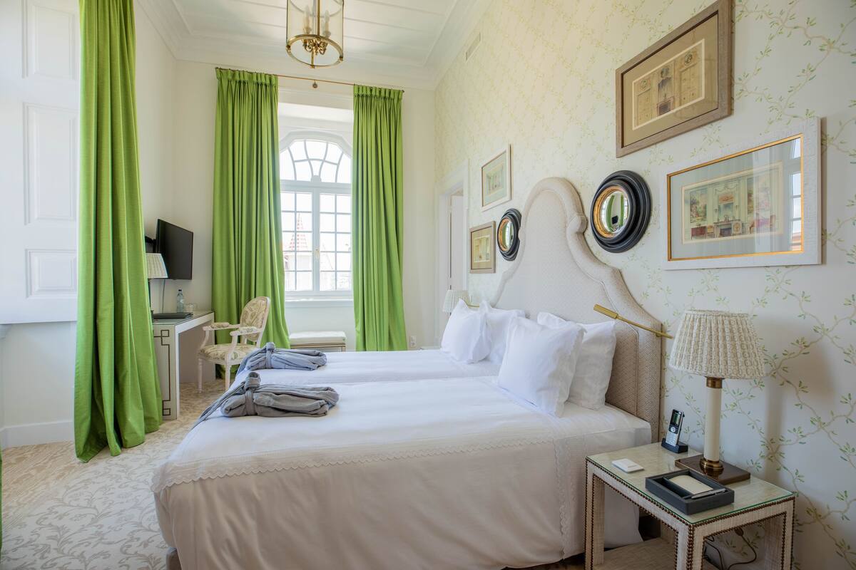 Een hotelkamer met twee bedden, een bureau met een computer, een stoel, een lamp en ingelijste foto’s aan de muur.