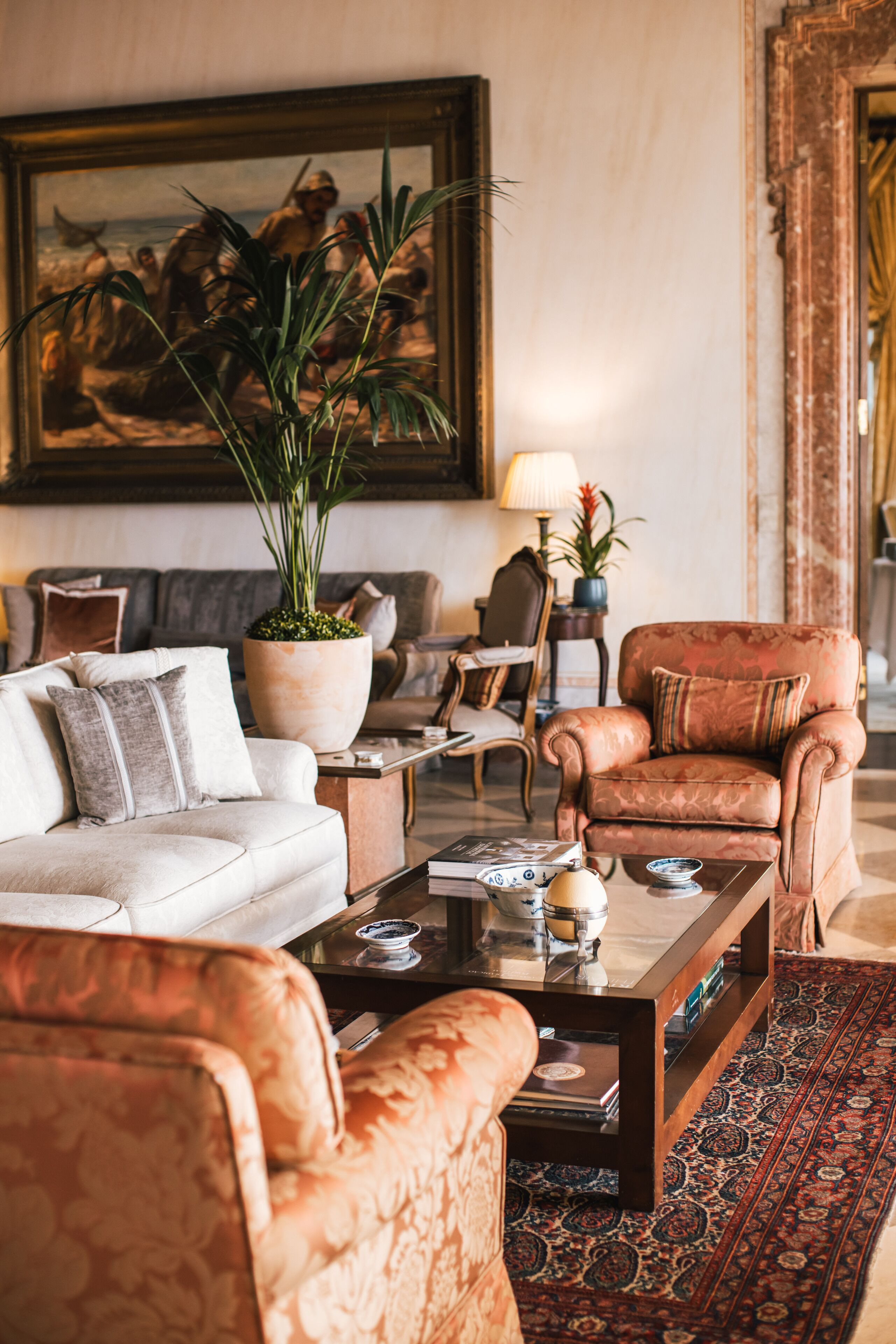 Uma sala de estar com sofá, poltrona, mesa de centro e uma planta grande em vaso.