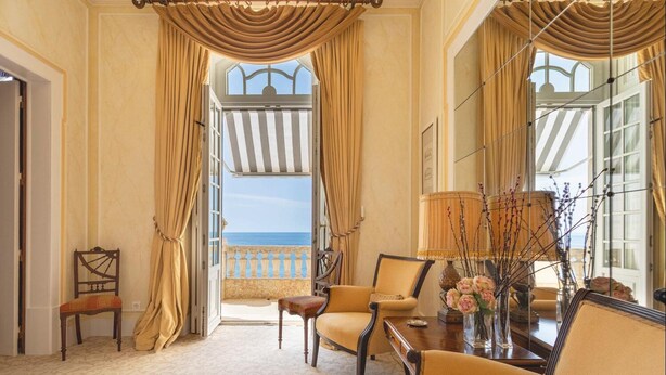Une chambre avec vue sur la mer, dotée d’un balcon, d’une table à manger avec des chaises et d’un vase rempli de fleurs.