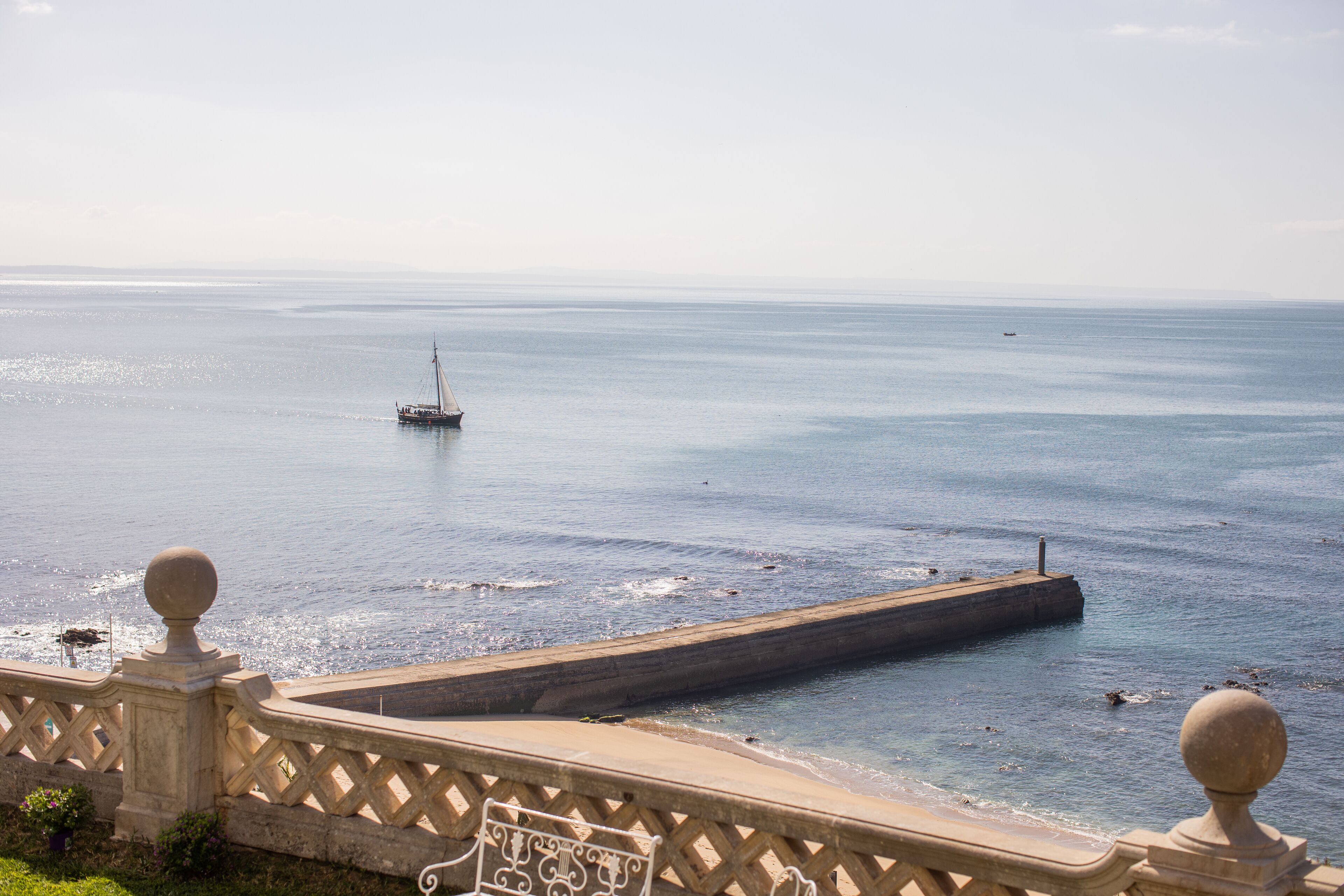 Vista sulla costa con un molo che si protende verso il mare, cielo sereno e balaustra in pietra.