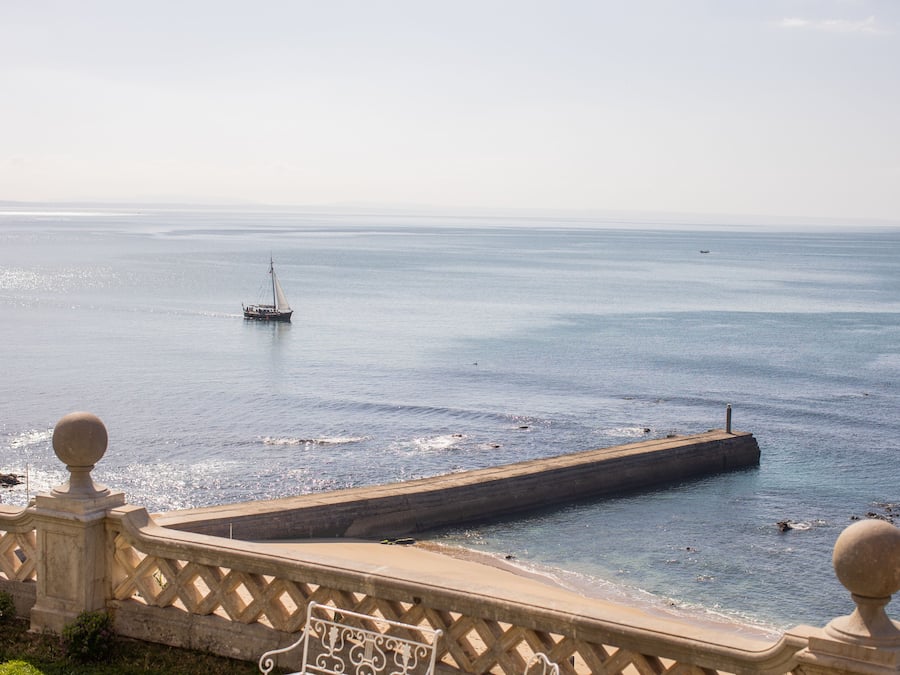 A coastal view with a pier extending into the sea, a clear sky, and a stone balustrade.