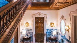 Un magnifique escalier orné de boiseries sculptées, un espace salon central avec des motifs décoratifs sur les tissus d’ameublement et un miroir décoratif.
