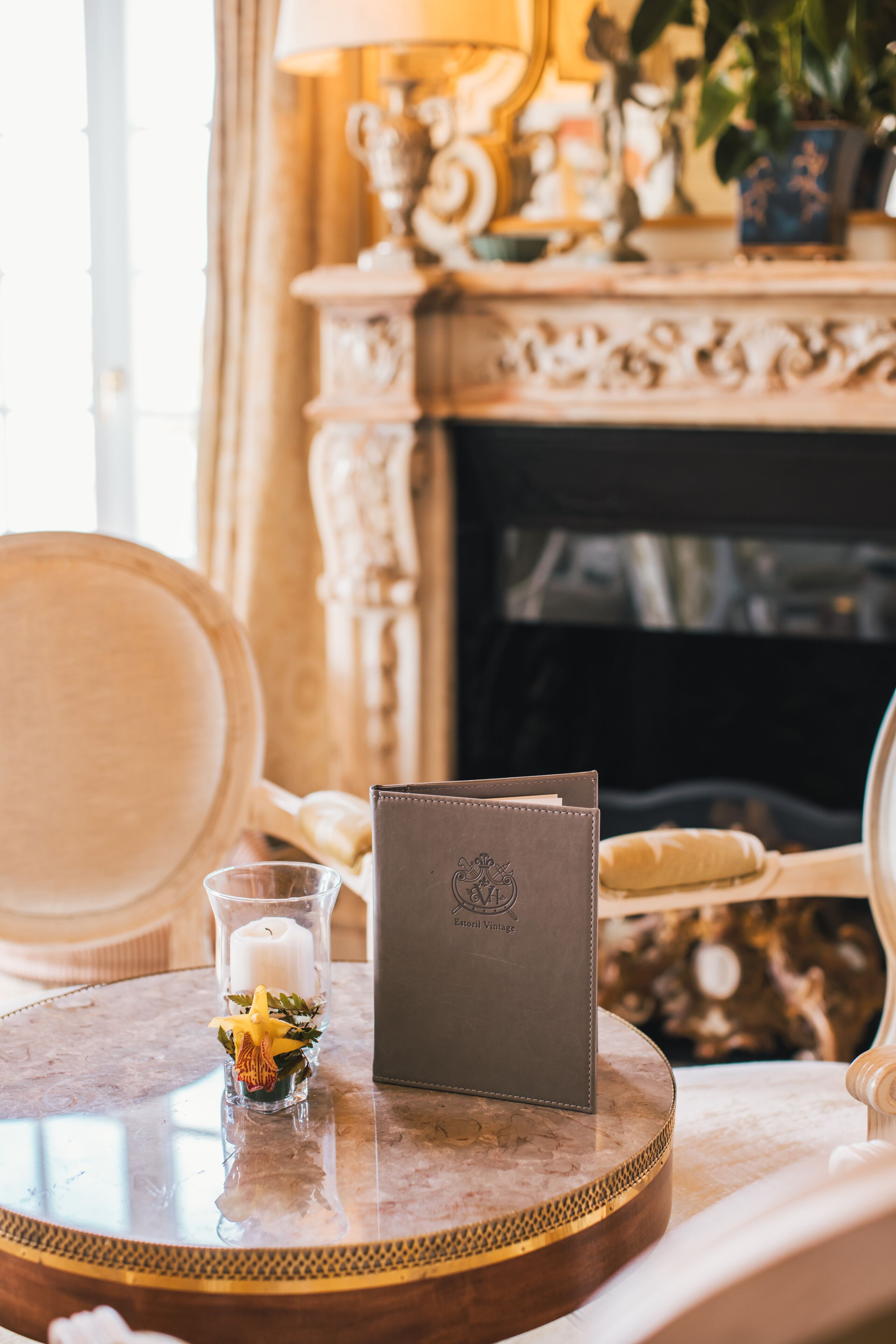 A round table with a leather wallet, a glass candle holder with a candle, and a small vase with flowers.
