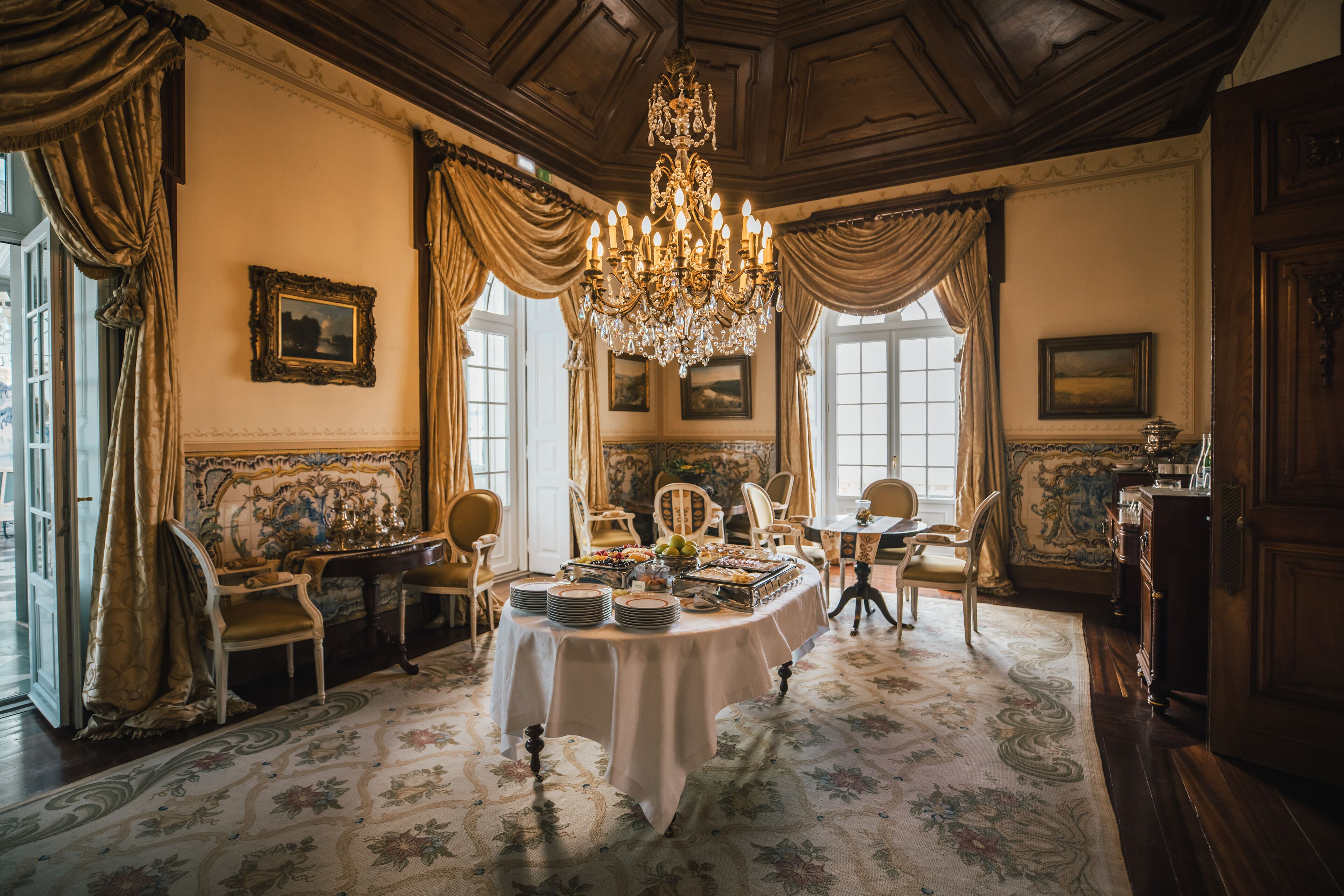 Un comedor formal con una araña, sillas ornamentadas y una mesa dispuesta para una comida.