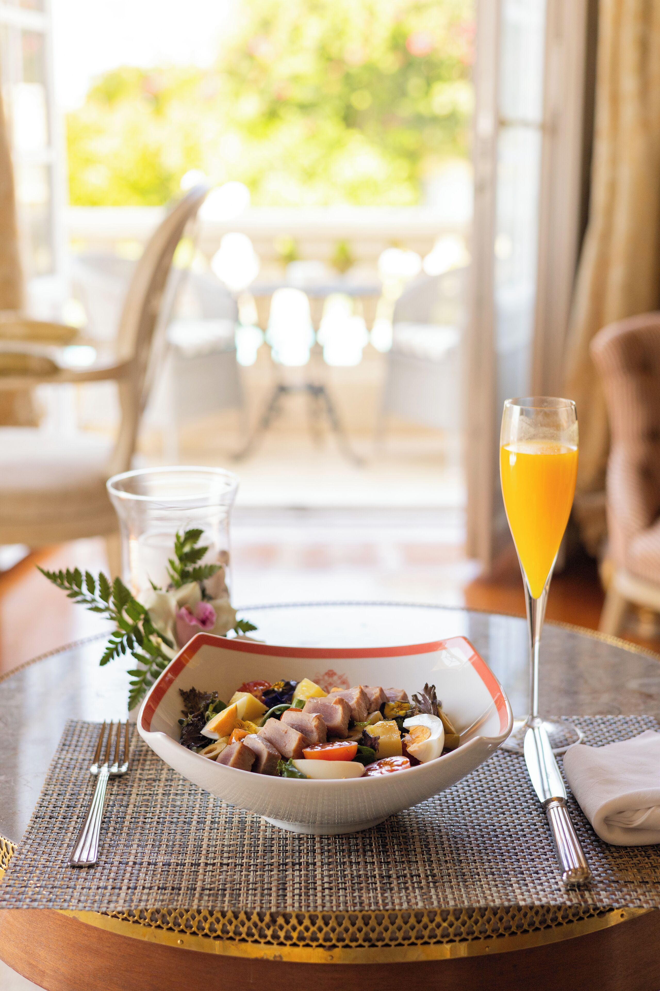 A dining table with a bowl of salad, a glass of orange juice, and a fork and knife on a placemat.