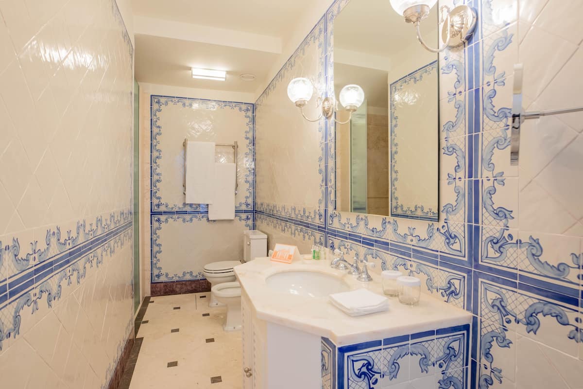 Ein Badezimmer mit einem weißen Waschbecken, blauen Zierfliesen, einem Spiegel und einer Toilette.