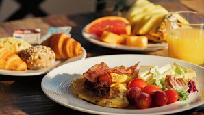 Una mesa de desayuno con platos de comida, incluyendo huevos, tocino, tomates, lechuga y jugo.