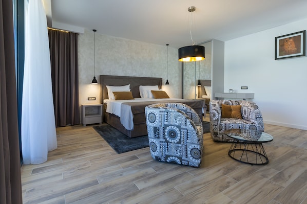 A modern hotel room with a bed, two patterned armchairs, a small table, a nightstand, a mirror, and a hanging light fixture. - Mirabilis Residence II (Zadar)