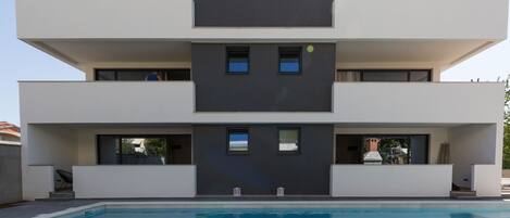 A modern multi-story building with a swimming pool in front.