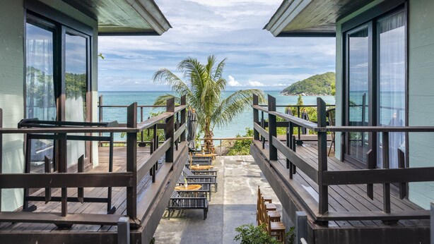Terraza de madera con mobiliario exterior con vistas a una playa y el océano.